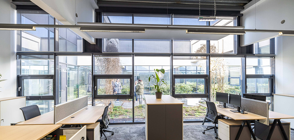 Mehrere PC-Arbeitsfläche vor einer Glasfront mit Blick in einem grünen Innenhof.