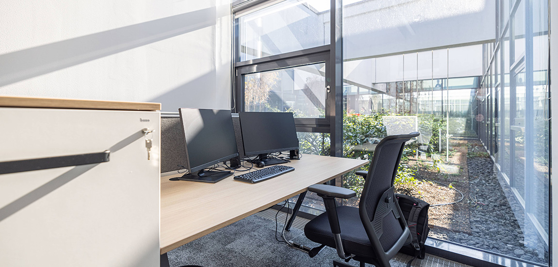 Seitlicher Blick auf einen PC-Arbeitsplatz mit einer Glasfront im Hintergrund.